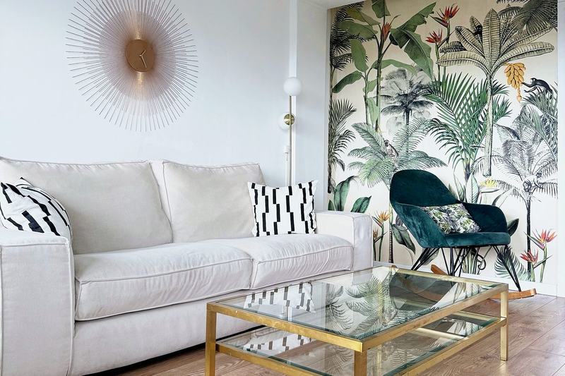 Bright living room with a beige sofa, a green armchair and tropical wallpaper