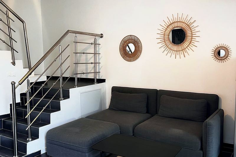 Living room with a grey sofa, a staircase and wicker mirrors