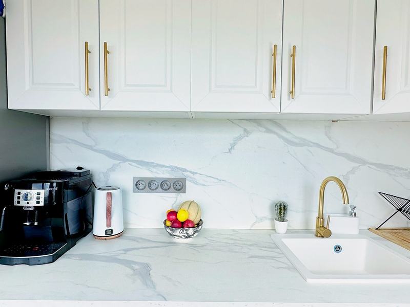 Fitted kitchen with a marble-effect worktop, a gold tap and a coffee machine
