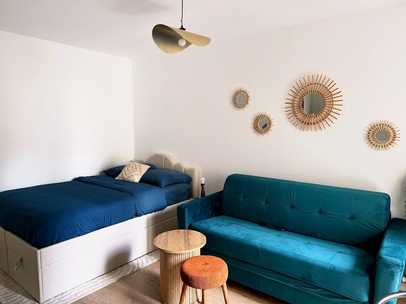 Bright main room with a bed, a teal sofa and sunburst mirrors